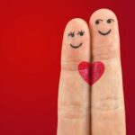 Index et majeur collés, avec un cœur au milieu. Des yeux et un sourire sur chacun des doigts, ils semblent amoureux.